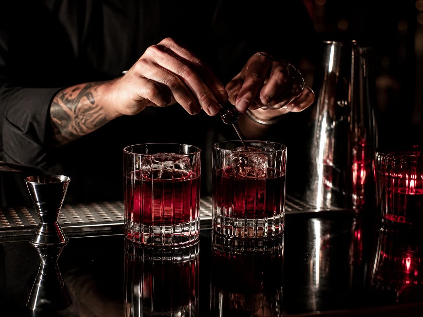 Bartender finishing two red cocktails at a polished black bar