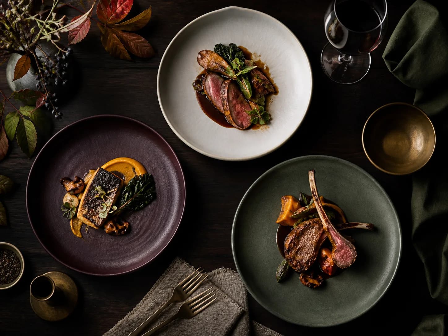 Three seasonal dishes arranged on a dark editorial table