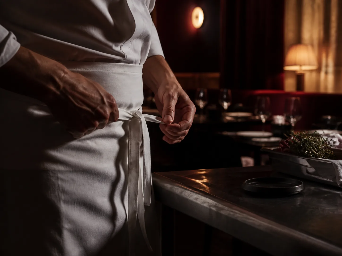 Chef tying a white apron beside the pass